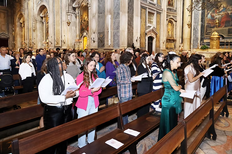 Pessoas em pé nos bancos da igreja, cantando e lendo partituras durante um culto.