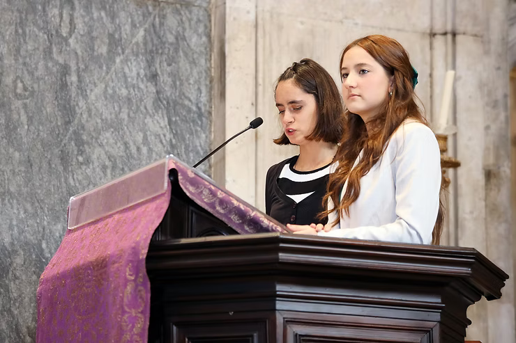 Duas mulheres discursando em um pódio com microfones em um salão com paredes de pedra.