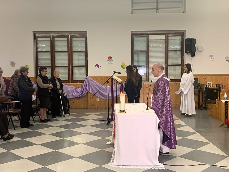 Padre com vestes roxas está em pé no altar durante o culto, com a congregação reunida nas proximidades.