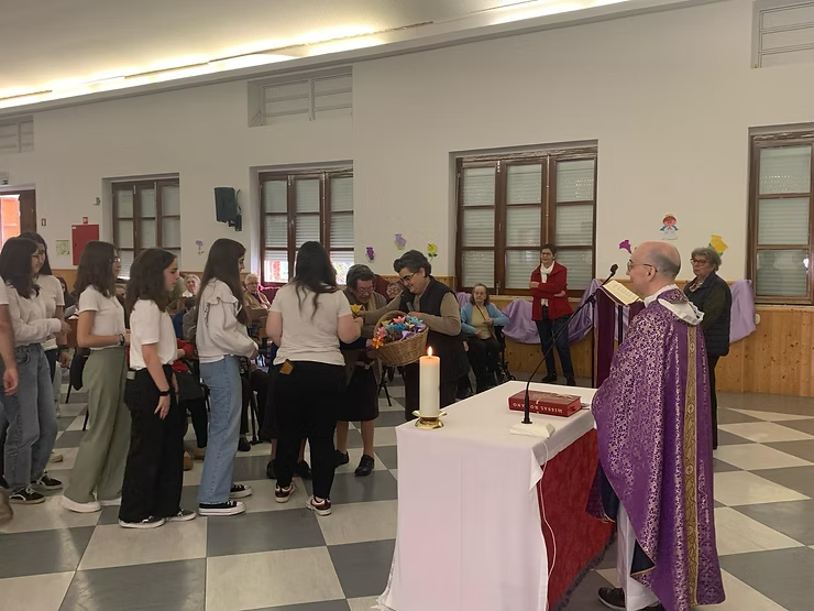 Padre com vestes roxas conduzindo um culto religioso perante uma congregação reunida.