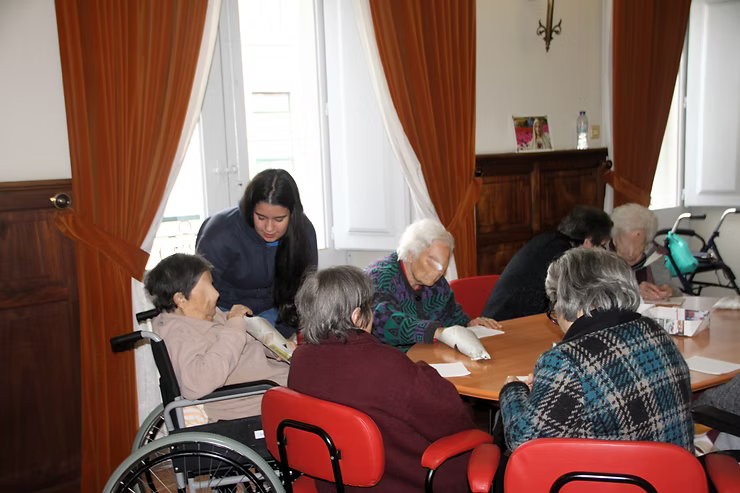 Pessoas sentadas ao redor de uma mesa em uma sala de reuniões, discutindo documentos com uma mulher em pé por perto.