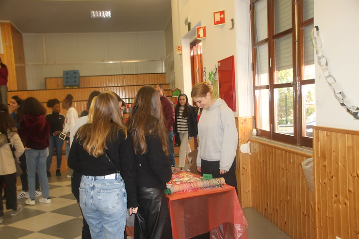 Alunos fazem fila no corredor da escola ao lado de uma mesa com papéis e uma mulher em pé por perto.