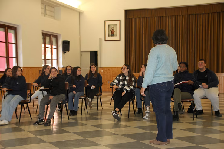 Pessoas sentadas em uma sala ouvem um orador que está em pé na frente de uma roda de reunião.