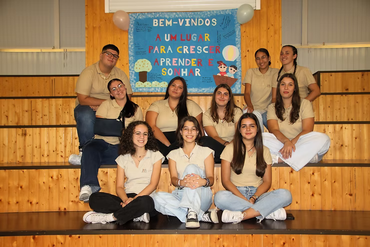Grupo de pessoas posando em uma academia sob uma placa de boas-vindas em uma parede de madeira.