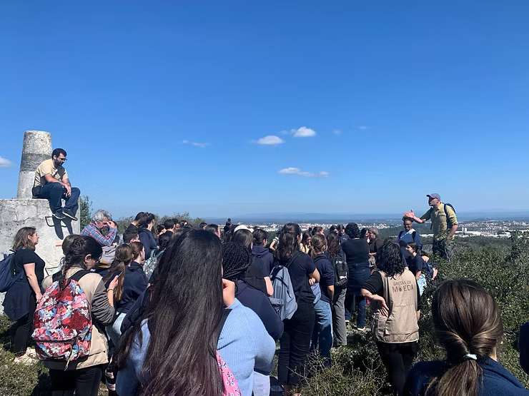 Uma multidão se reuniu em um mirante panorâmico sob um céu azul claro, com as pessoas voltadas para a vista.