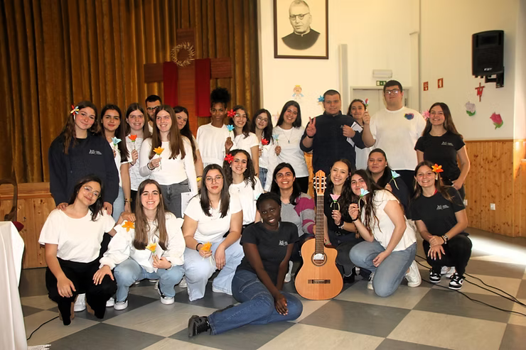 Grupo posando em ambiente interno com um violão, em frente a uma cortina e um retrato.
