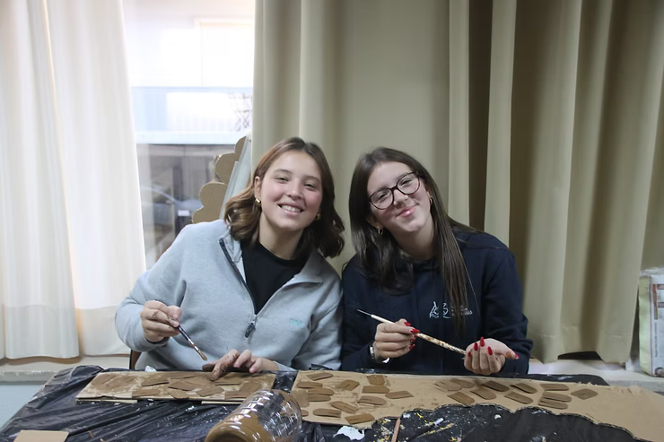 Duas pessoas sorridentes sentadas à mesa, segurando pauzinhos, com um tecido estendido à sua frente.