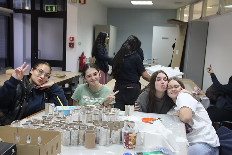 Pessoas posando ao redor de uma mesa com xícaras em uma sala iluminada, com outras trabalhando ao fundo.
