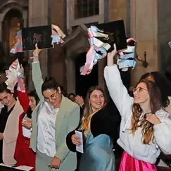 Pessoas vibrando e agitando pastas pretas em uma festa de formatura noturna.