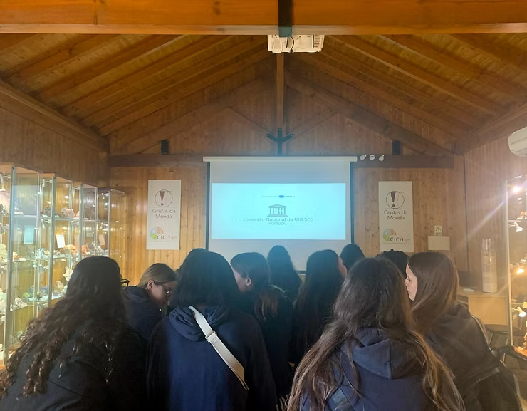 Os alunos reuniram-se num salão de madeira para assistir a uma apresentação num ecrã de projeção.