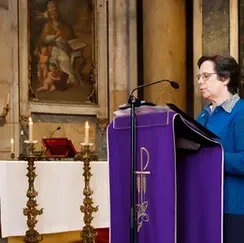 Pessoa discursando em um púlpito roxo no interior de uma igreja iluminada por velas.