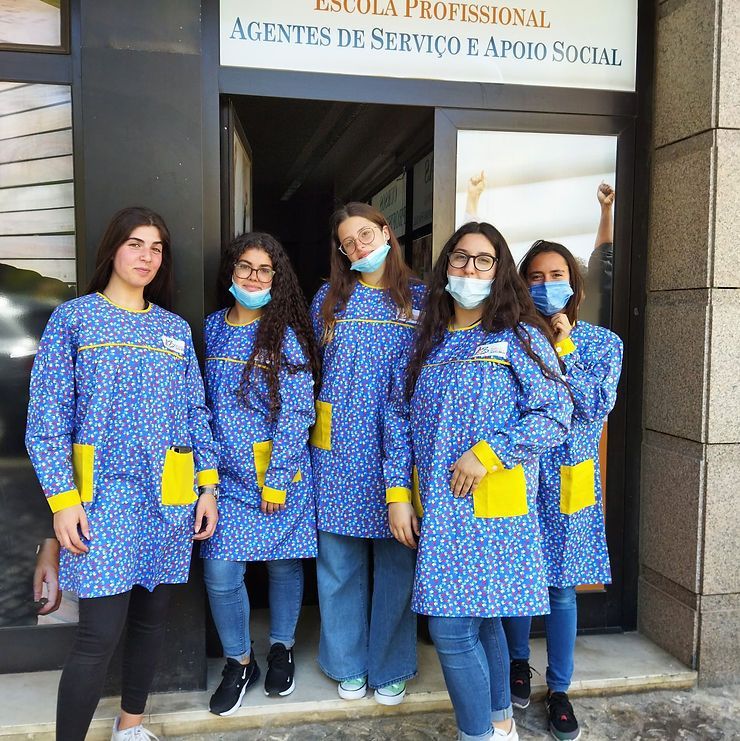 Cinco pessoas vestindo uniformes azuis iguais estão em pé do lado de fora da placa de entrada de uma escola.