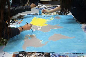 Pessoas pintando juntas um grande mapa-múndi em papel azul.