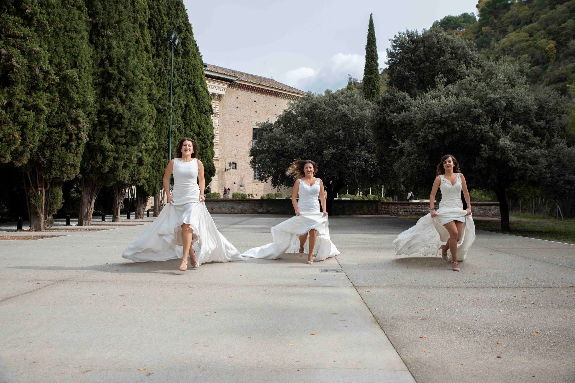 Tres mujeres con vestidos blancos corren por una calle.