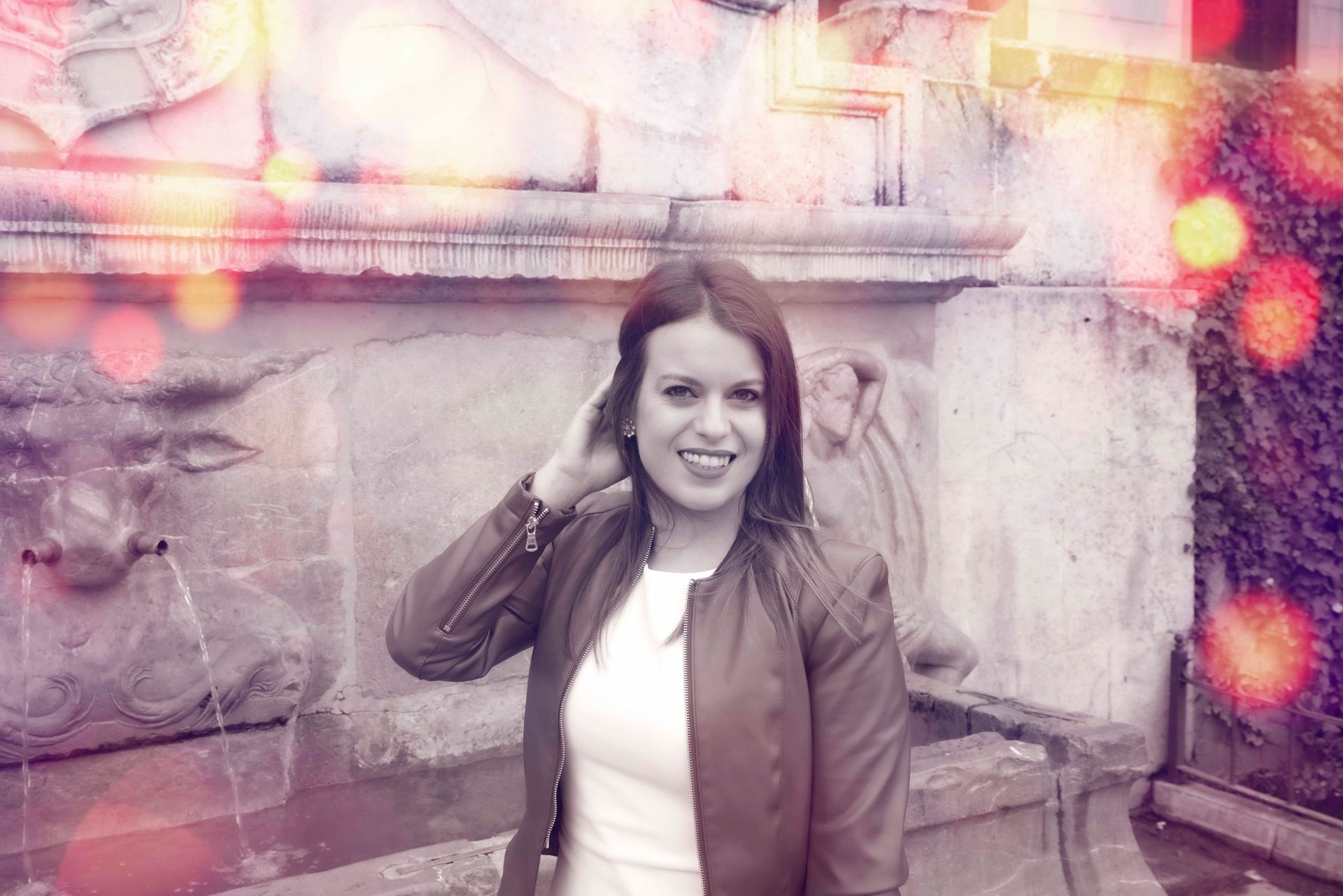 Una mujer con una chaqueta marrón está parada frente a una fuente.