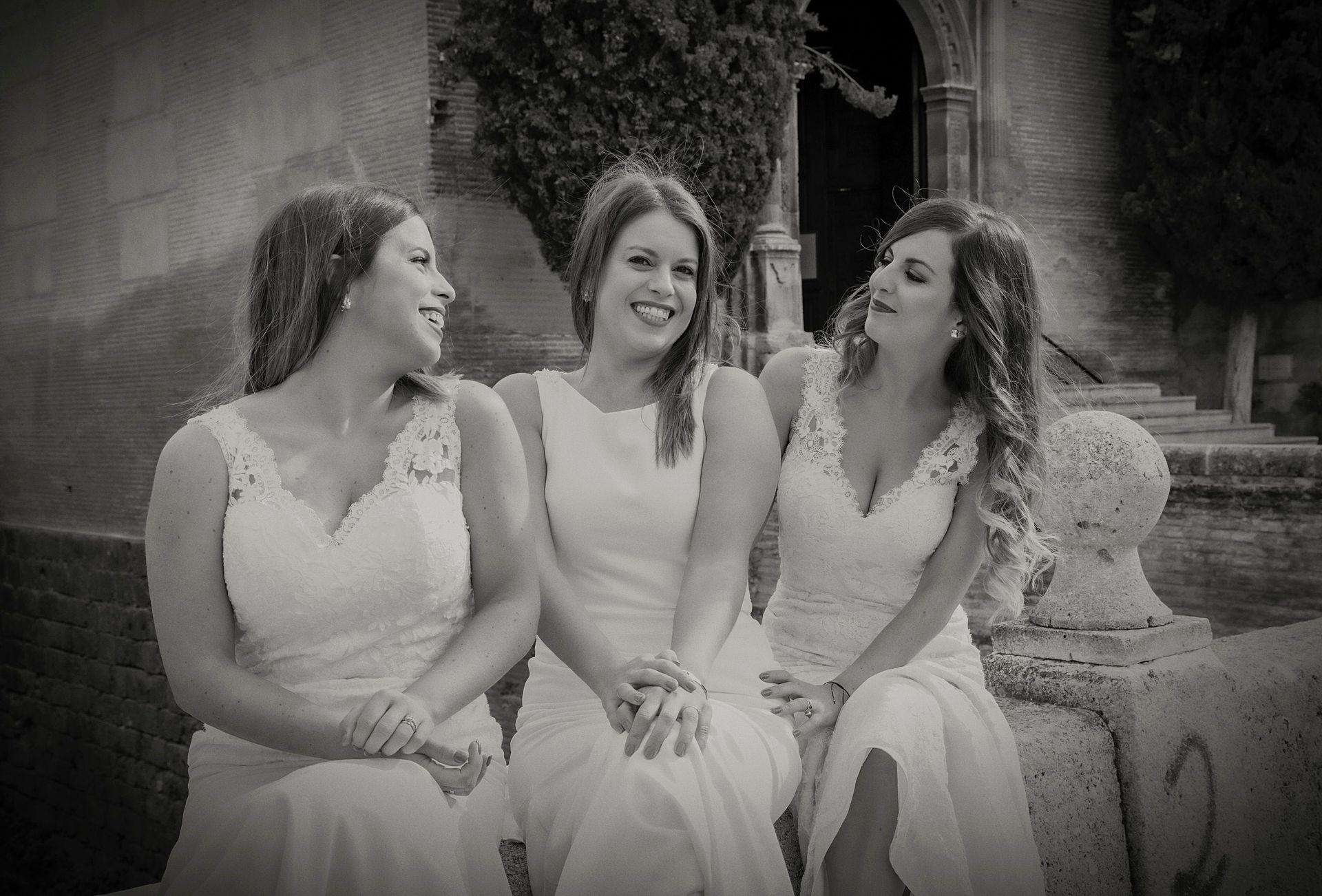 Tres mujeres con vestidos blancos están sentadas una al lado de la otra frente a un edificio.
