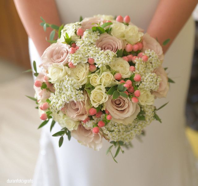 Una mujer con un vestido blanco sostiene un ramo de flores rosas y blancas.