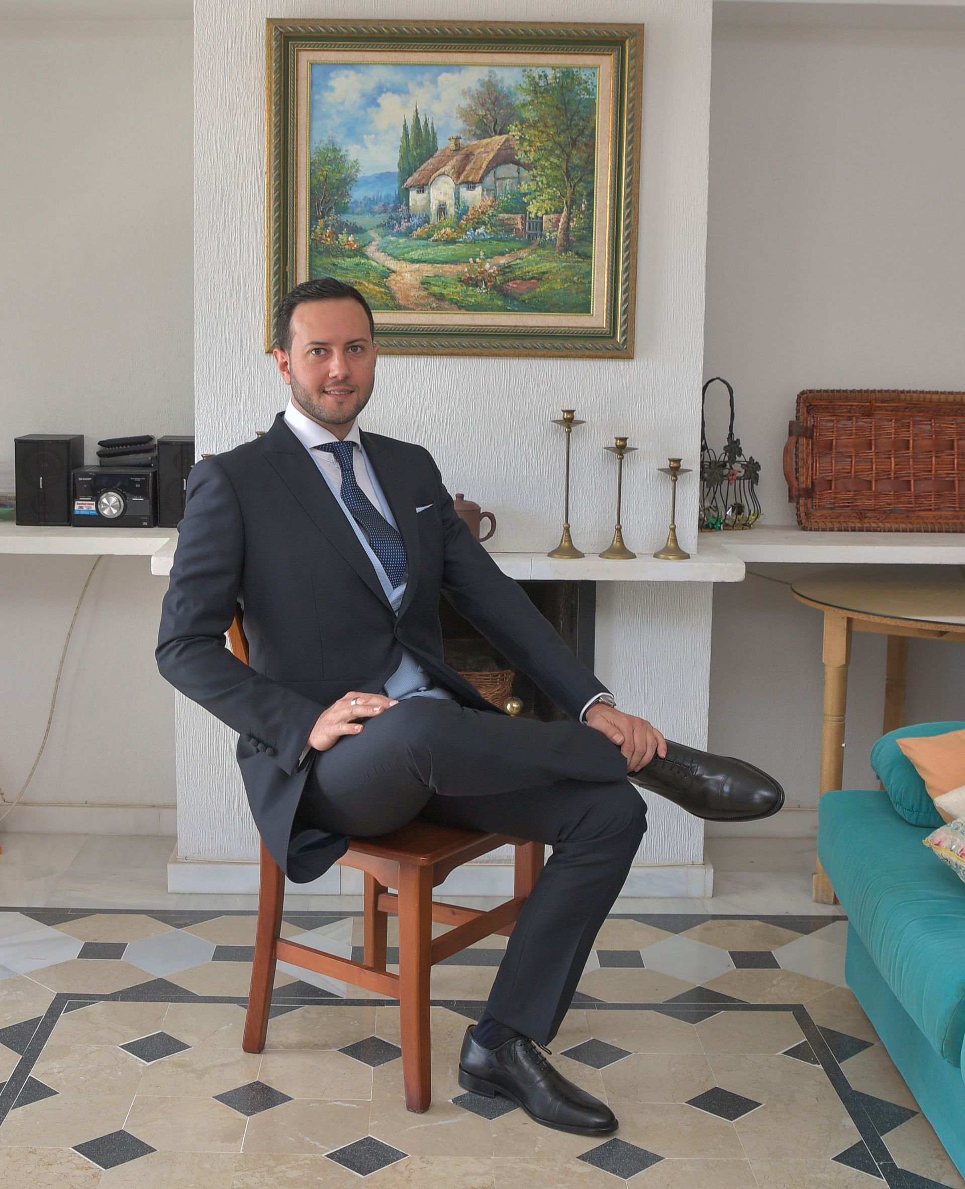 Un hombre con traje y corbata está sentado en una silla en una sala de estar.