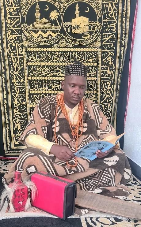 Hombre abraza a persona con camisa naranja, sonriendo ampliamente. Al aire libre, con palmeras al fondo.