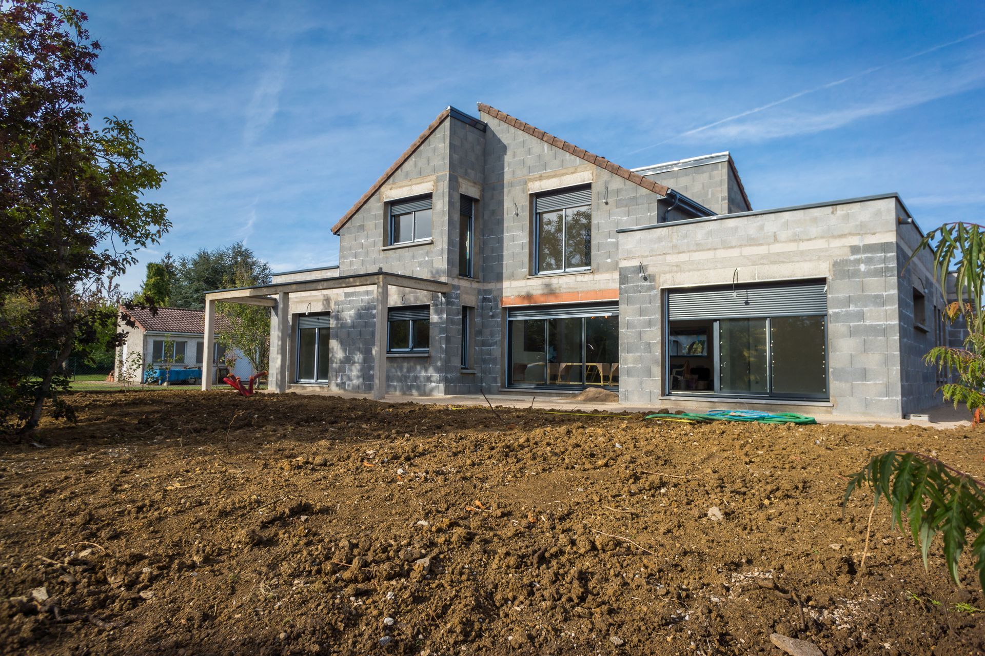 Maison moderne en pierre en construction avec de grandes fenêtres et un devant en terre battue.