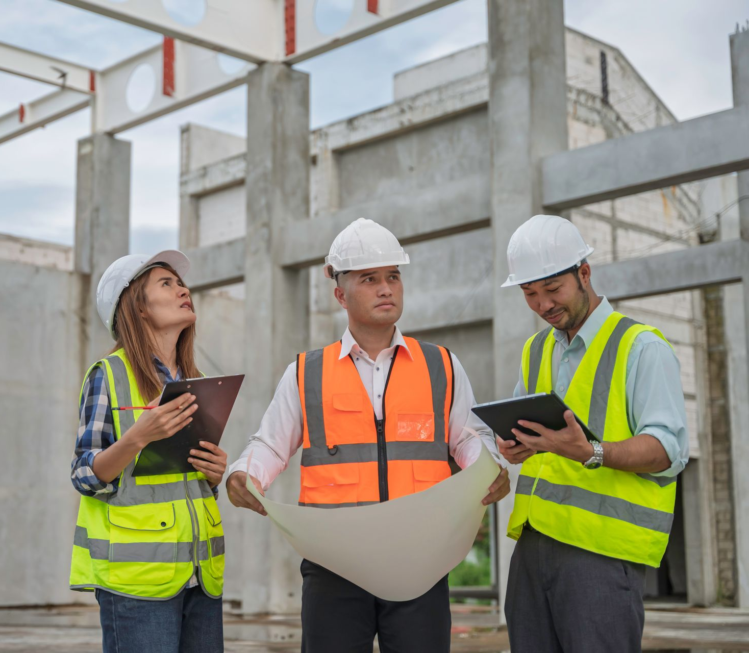 Trois ouvriers du bâtiment, casqués et vêtus de gilets de sécurité, examinent des plans sur un chantier.