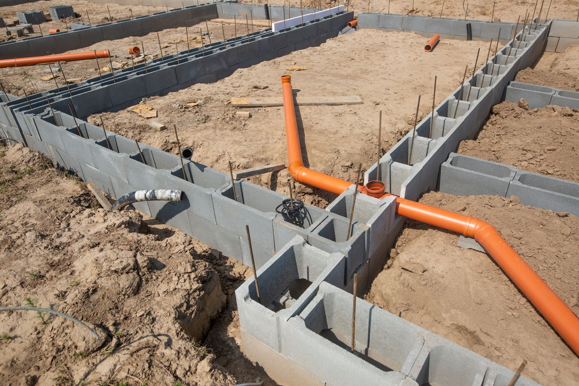 Fondations partiellement construites avec des blocs de béton et une canalisation sur un chantier sablonneux.