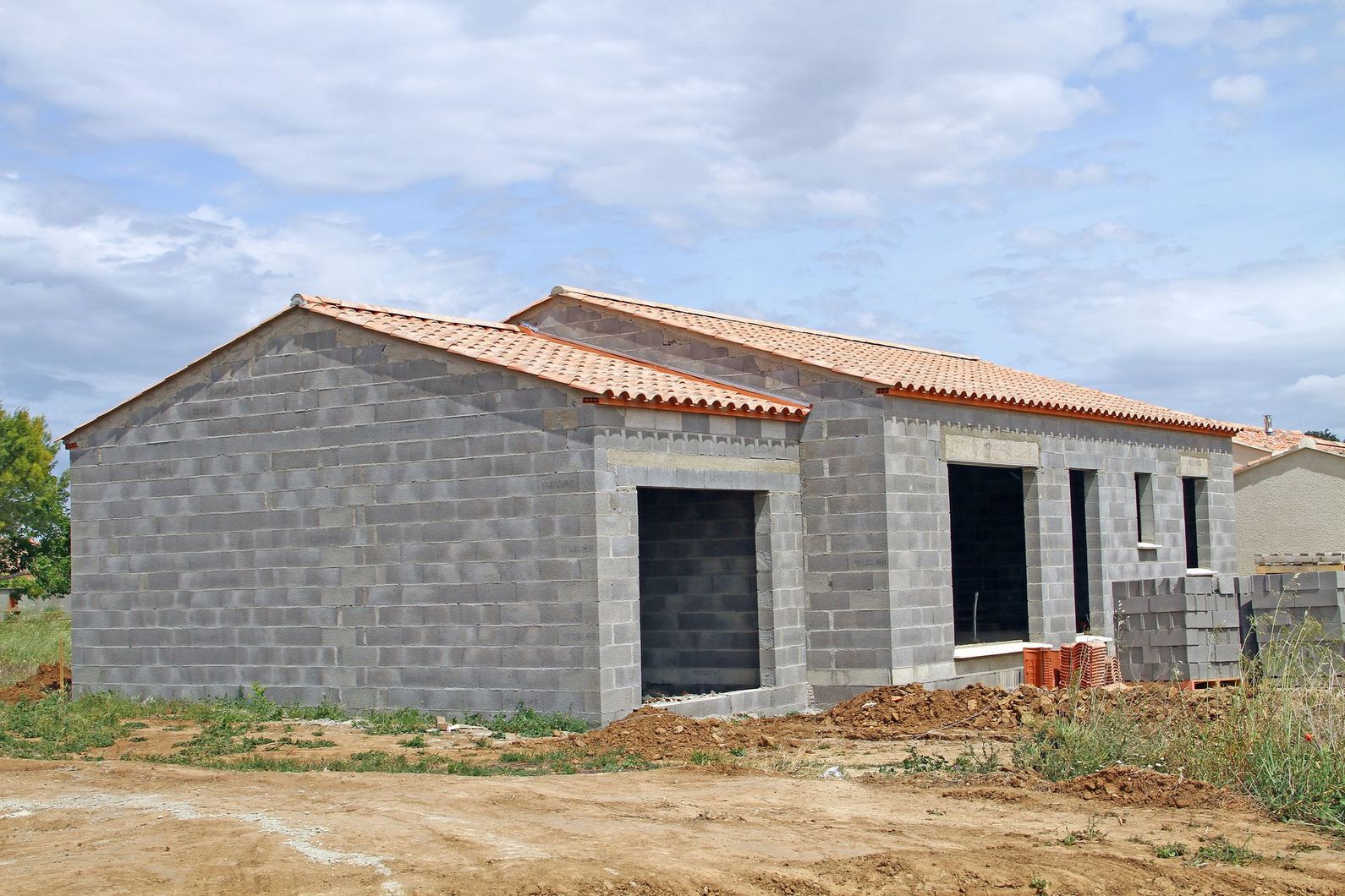 Maison inachevée en briques avec un toit de tuiles sur un terrain vague.