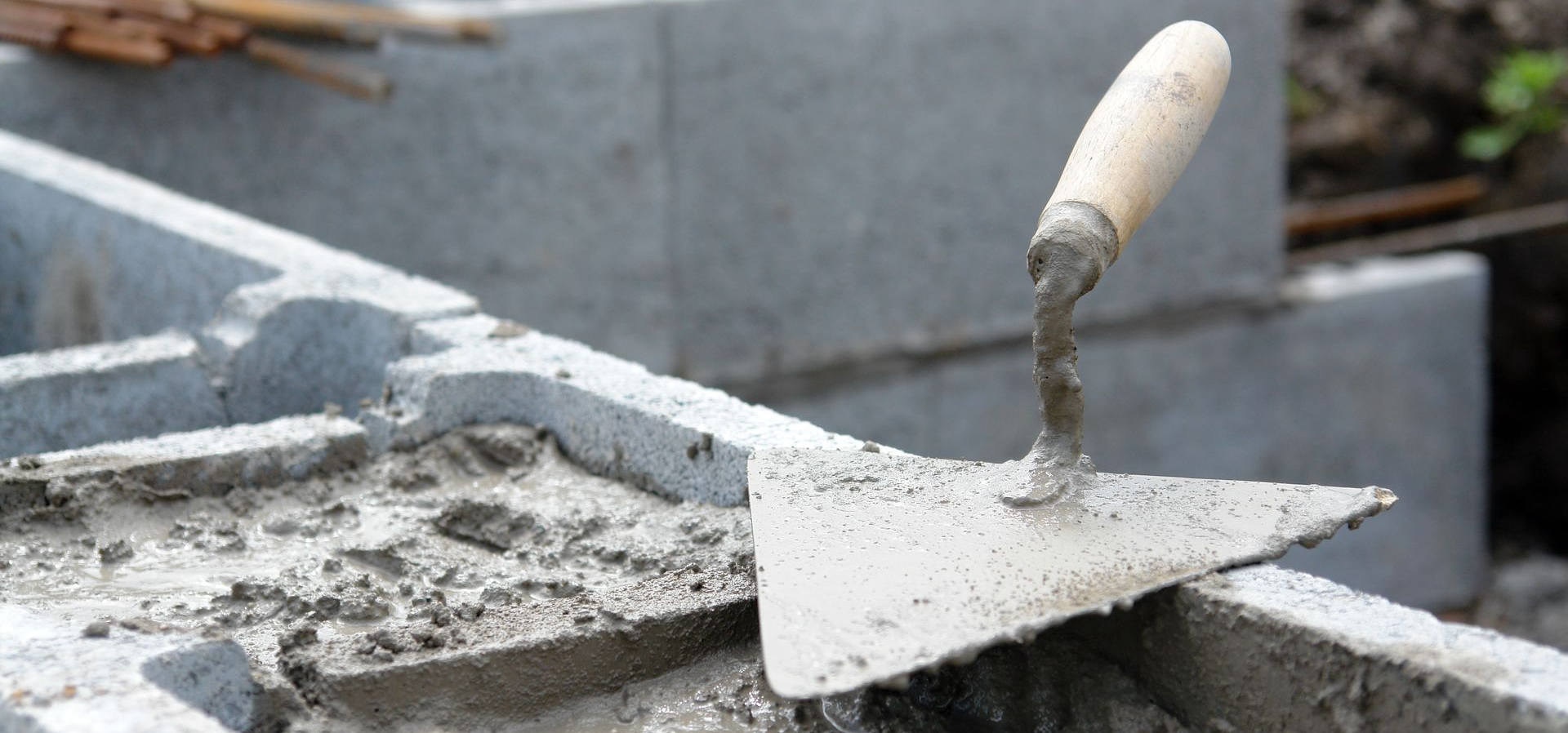 Truelle de chantier posée sur du béton frais dans une brouette ou une auge à mélanger.
