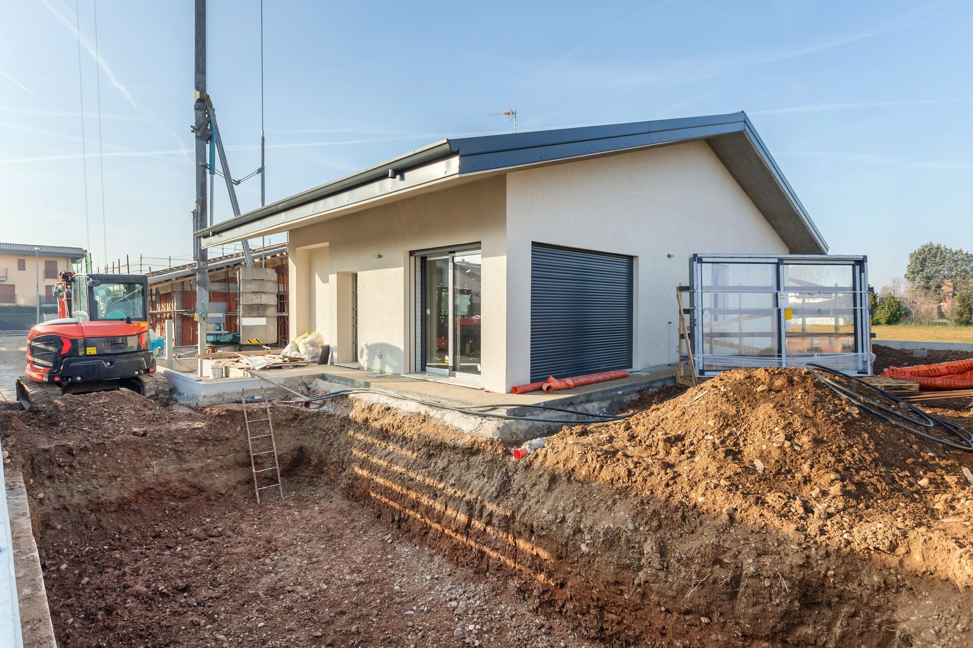 Maison neuve en construction, avec des tas de terre, un toit et une petite voiture à proximité.