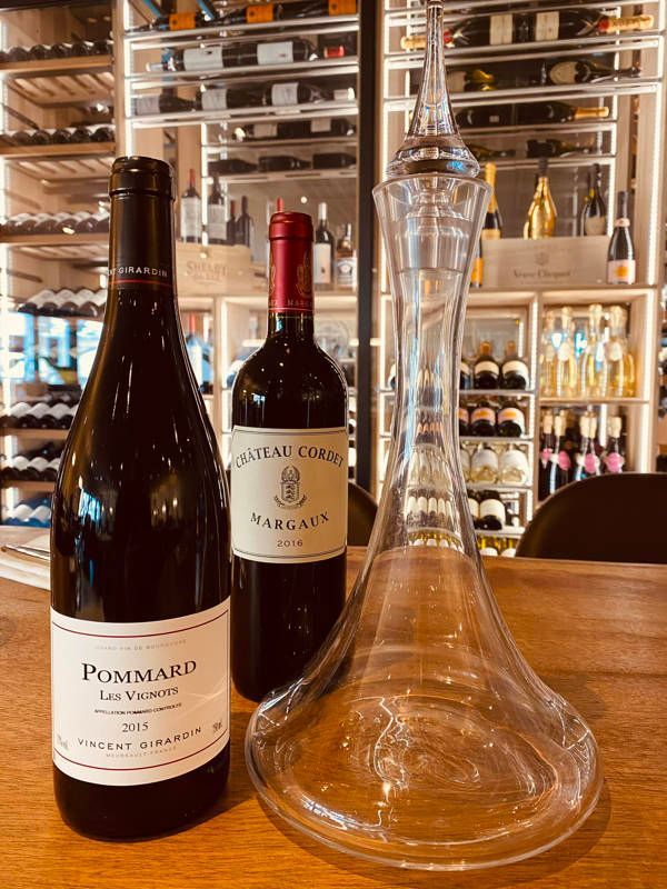 Une table avec bouteilles et carafe au premier plan, dans le fond une cave à vin vitrée dans un restaurant