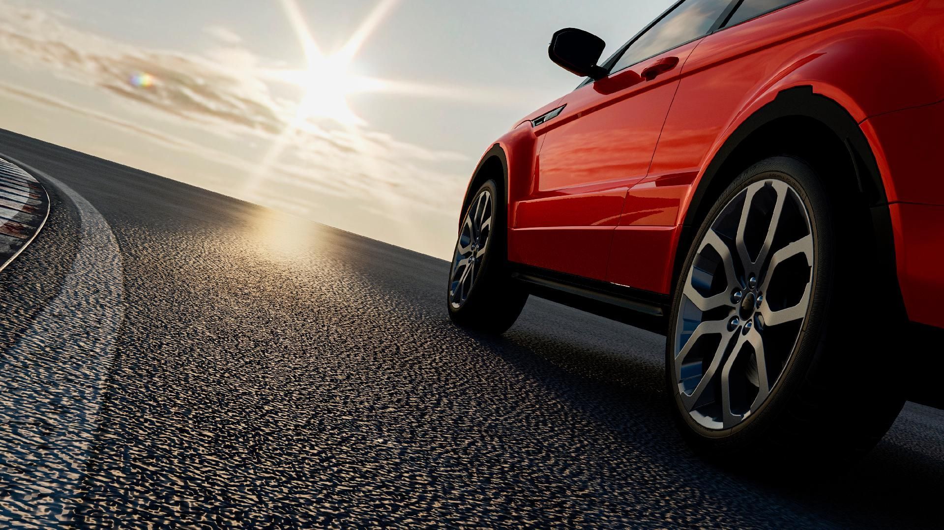 Ein roter Sportwagen fährt bei Sonnenuntergang auf einer sonnenbeschienenen Straße.