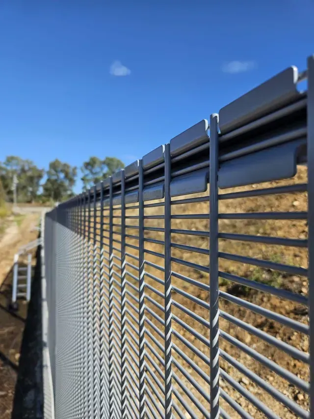 Primer plano de una valla de seguridad metálica alta y gris contra un cielo azul.