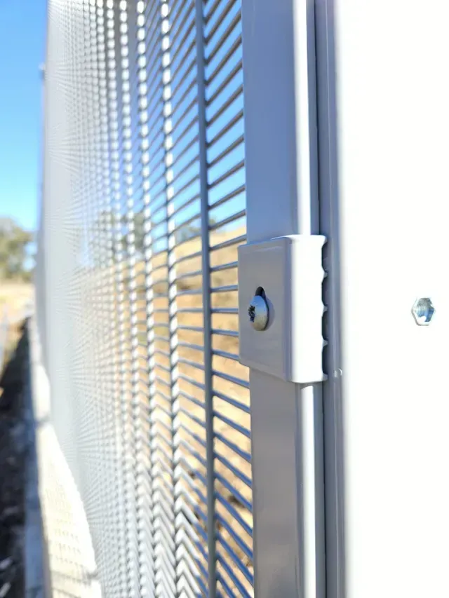 Primer plano de un detalle de una valla de seguridad con un panel de rejilla de metal y un pestillo cerrado.