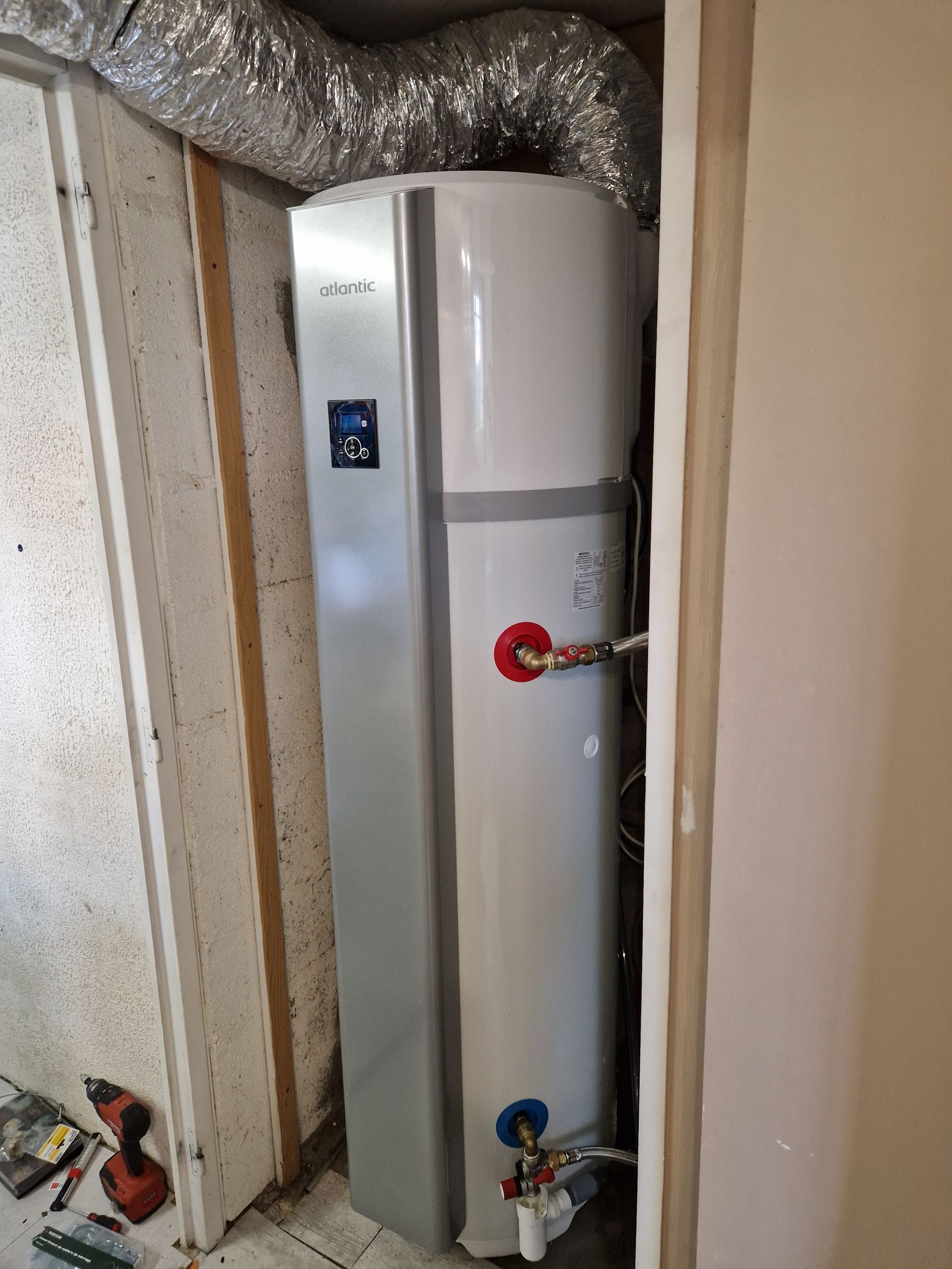 Grand chauffe-eau blanc dans un placard technique avec des conduits argentés.