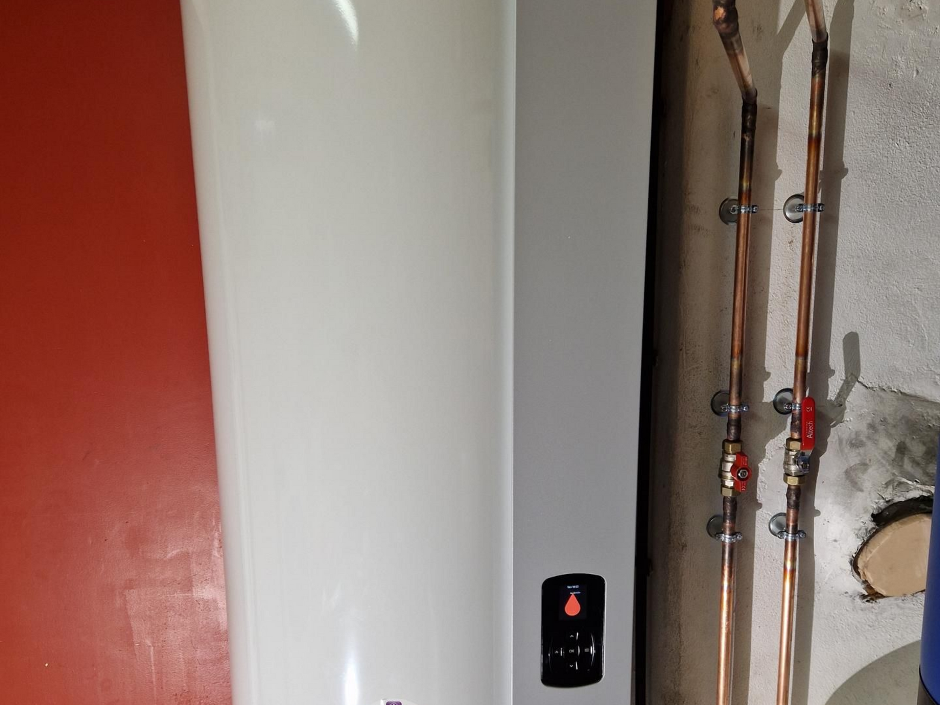 Un chauffe-eau White Atlantic, à côté de tuyaux en cuivre et d'une porte rouge.