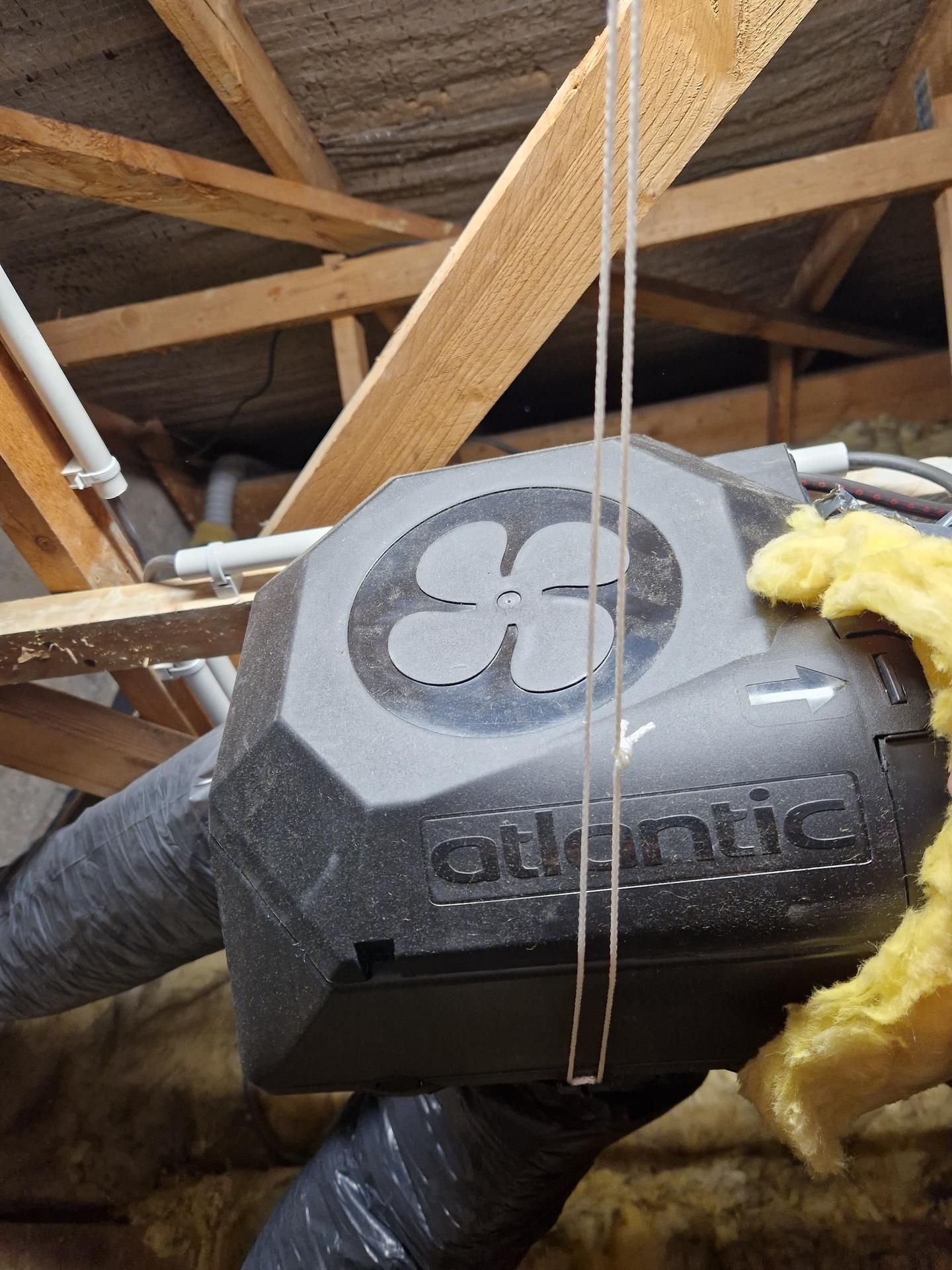 Un système de ventilation, étiqueté Atlantic, installé dans un grenier avec poutres en bois et isolation.
