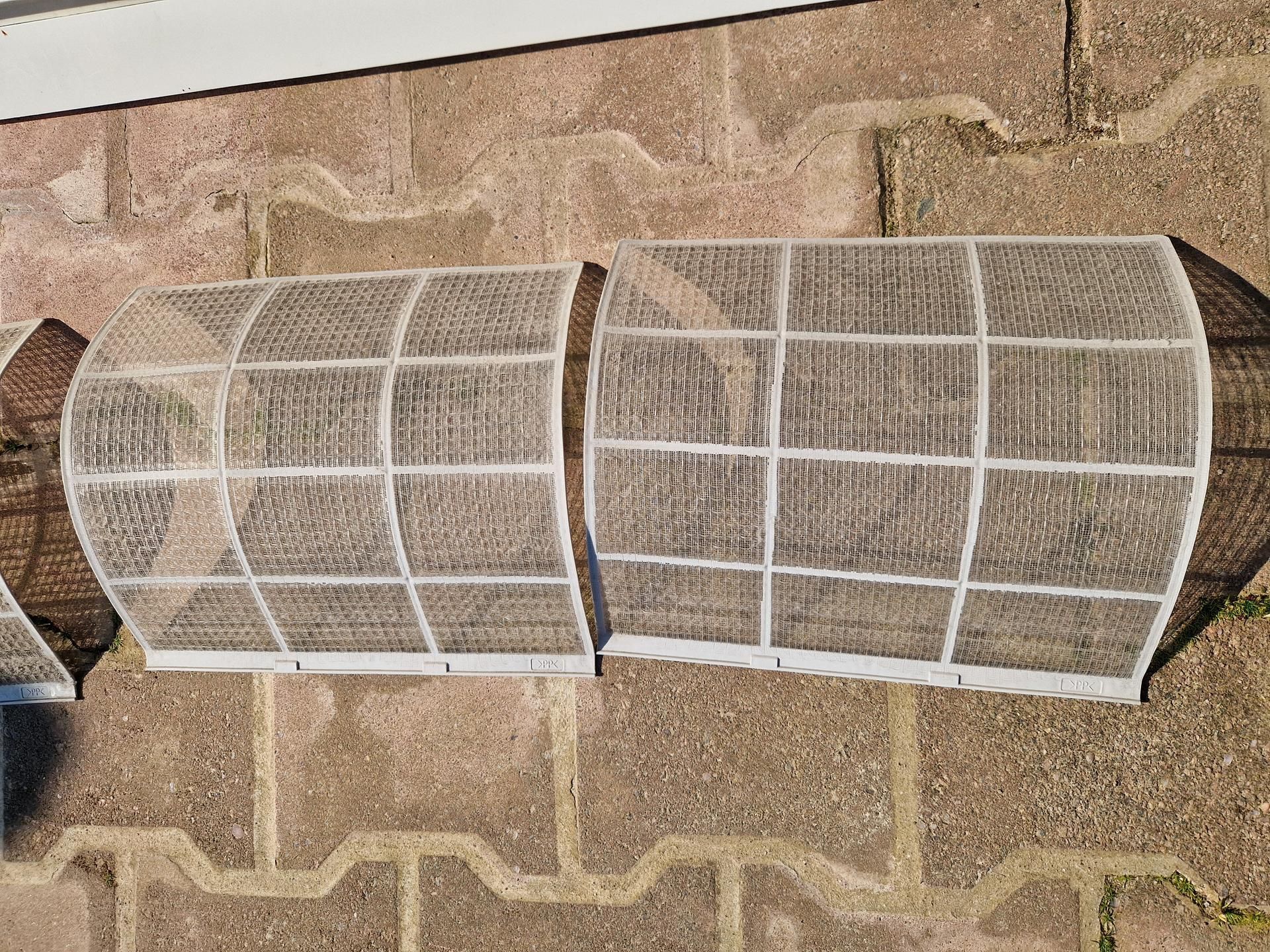 Deux filtres de climatiseur rectangulaires posés sur une surface en briques.