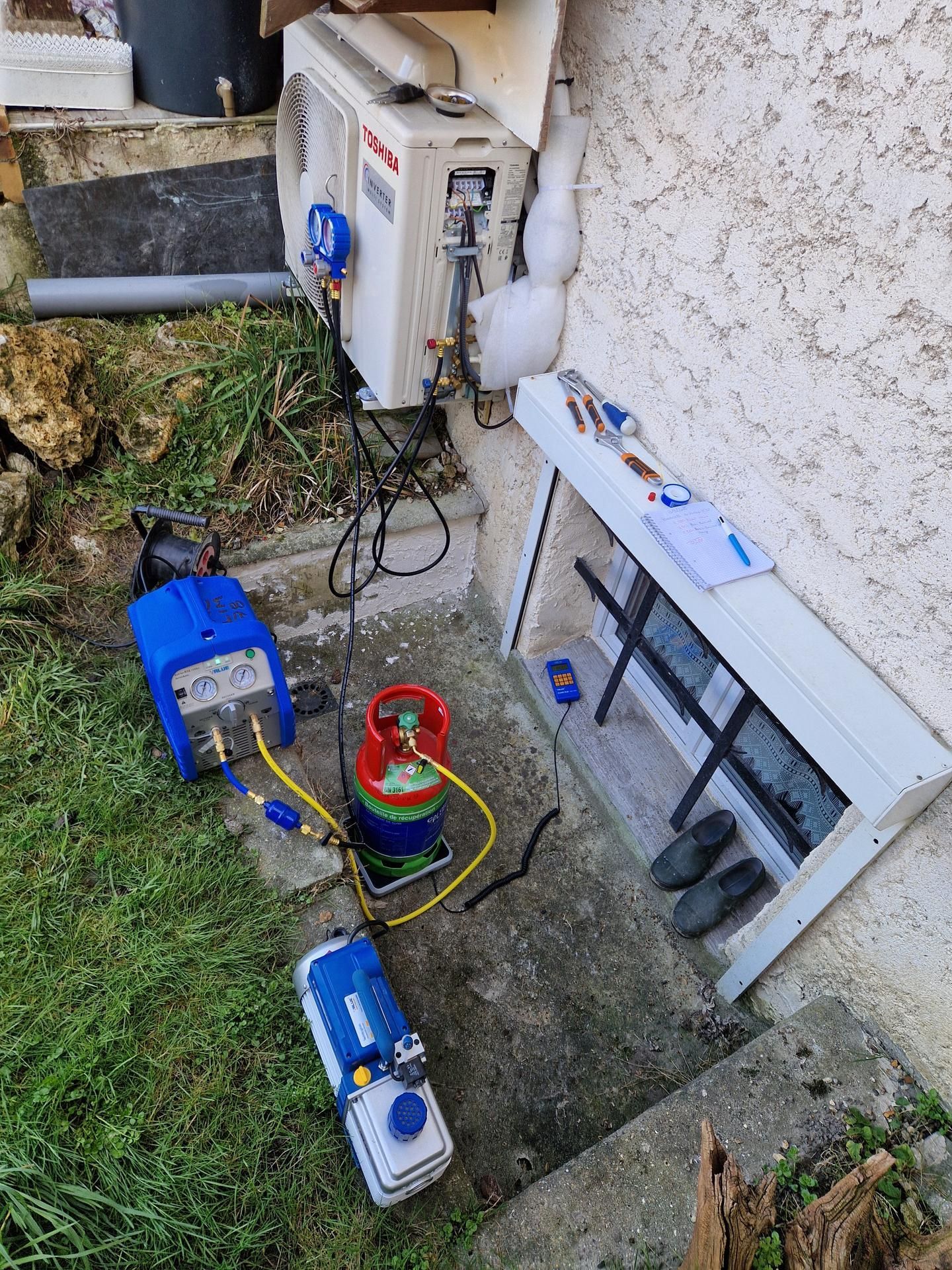 Installation du matériel CVC pour réparation : pompe à vide bleue, réservoir de réfrigérant, manomètres et unité de climatisation extérieure.