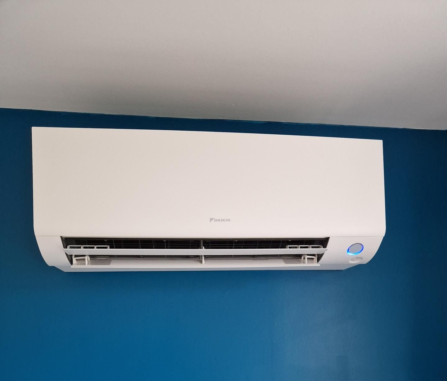 Unité de climatisation blanche fixée sur un mur bleu.