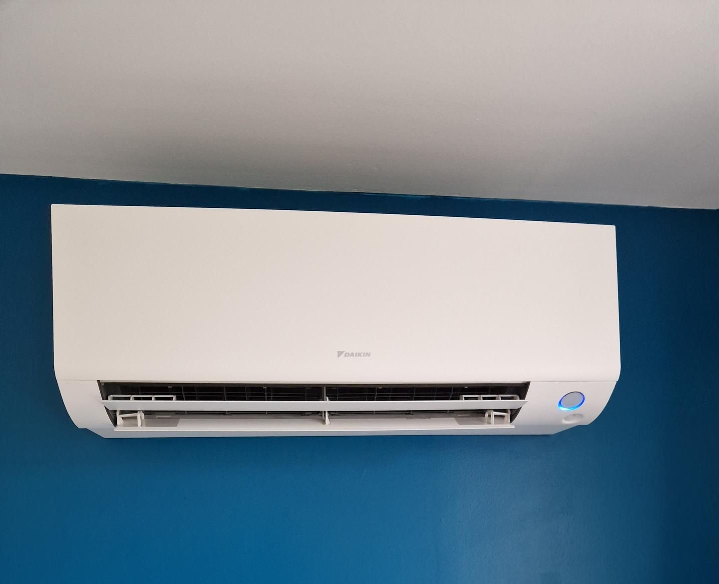 Unité de climatisation blanche fixée sur un mur bleu.