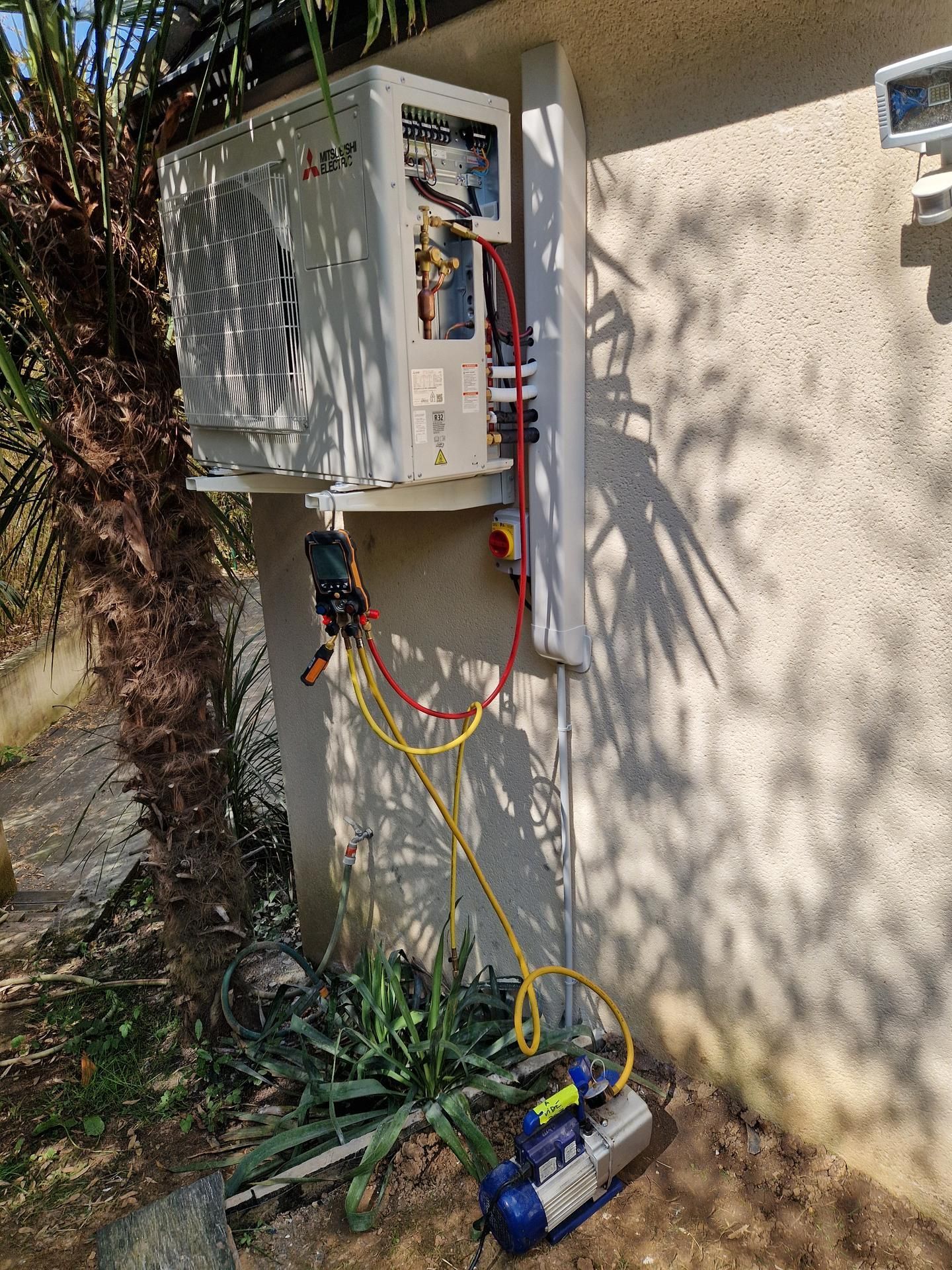 Un climatiseur en cours d'entretien à l'extérieur, avec des tuyaux reliés à une pompe à vide.