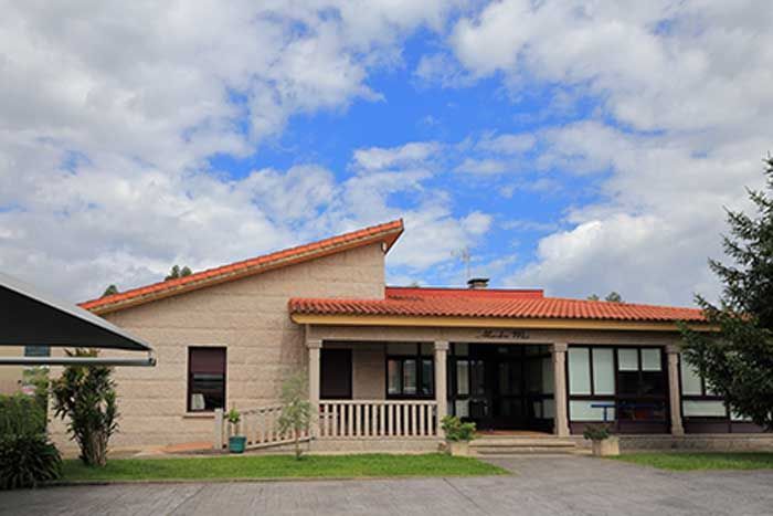 Una casa grande con techo de tejas rojas está ubicada encima de un exuberante campo verde.