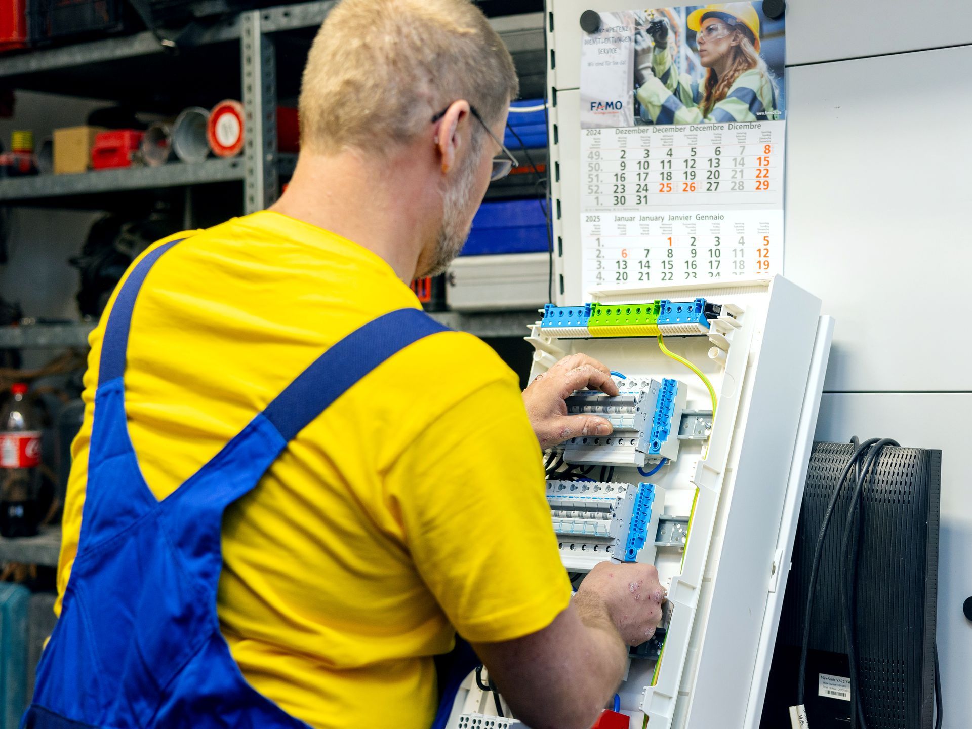 Ein Elektriker in einem gelben Hemd und einem blauen Overall arbeitet an einer Schalttafel