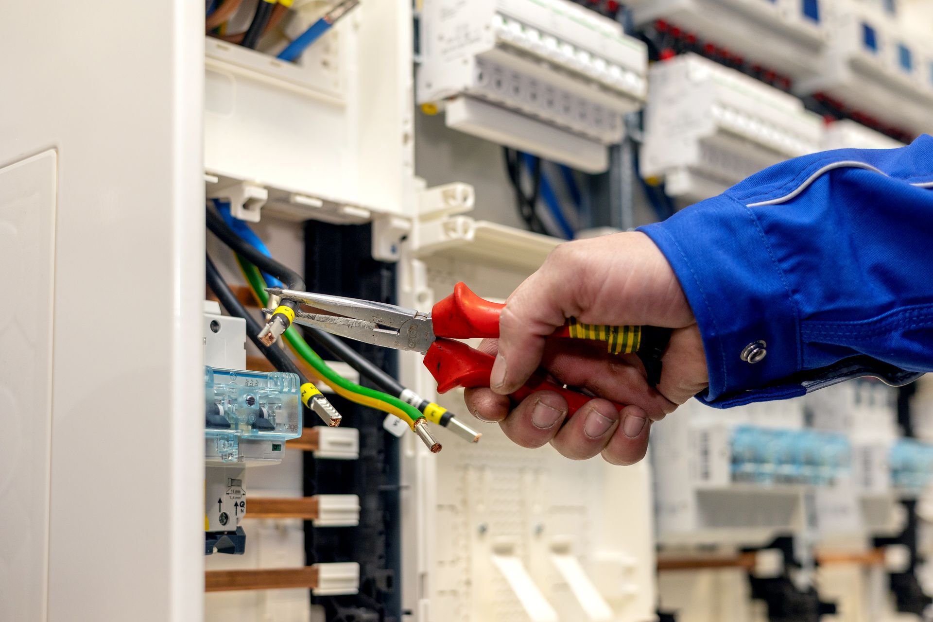 Eine Elektriker arbeitet mit einer Zange an einem Schaltkasten