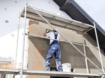 Ein Mann steht auf einem Gerüst und streicht eine Hauswand.