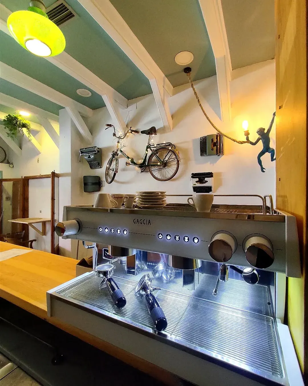 Cafetera de café expreso en una cafetería. Arte de una bicicleta y un mono en la pared. Vigas de madera, luz amarilla.