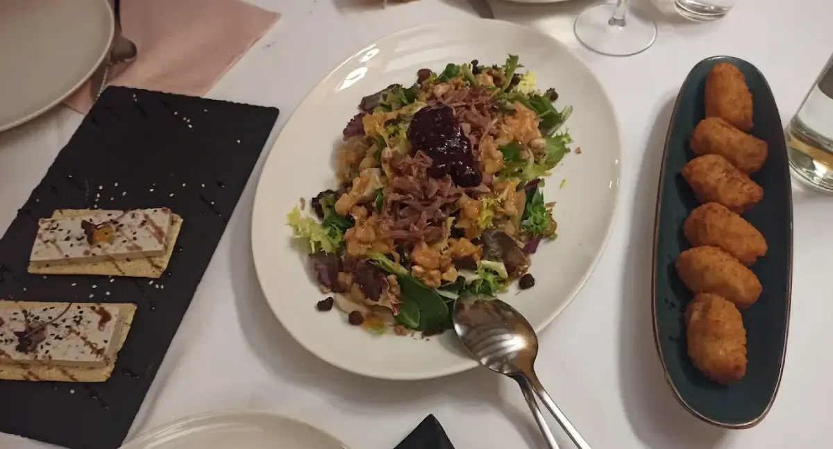 Plato de ensalada con cuchara, croquetas y pasteles sobre una mesa.