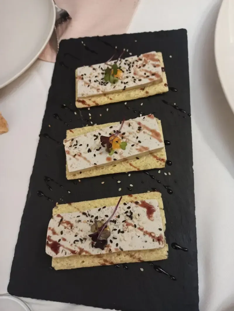 Tres aperitivos rectangulares sobre una pizarra negra. Cada uno tiene un diseño en capas, con pan tostado y cobertura blanca.