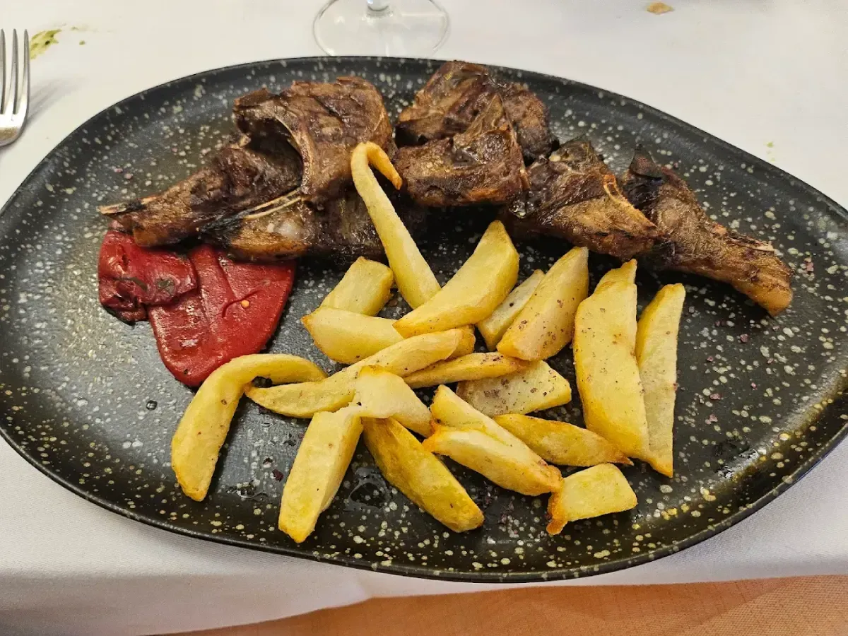 Chuletas de cordero con patatas fritas y pimiento rojo asado en un plato negro moteado.