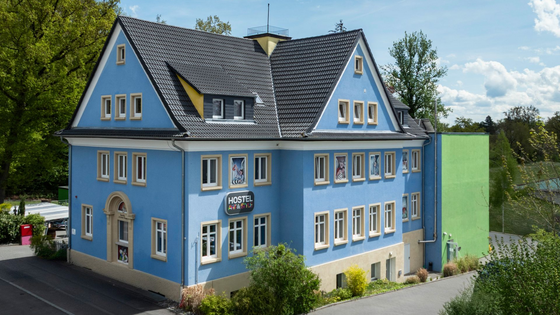 Blaues Gebäude mit dunklem Dach; „Route 66“-Schild, Fenster, grüne Seite, gelbe Akzente, Bäume.